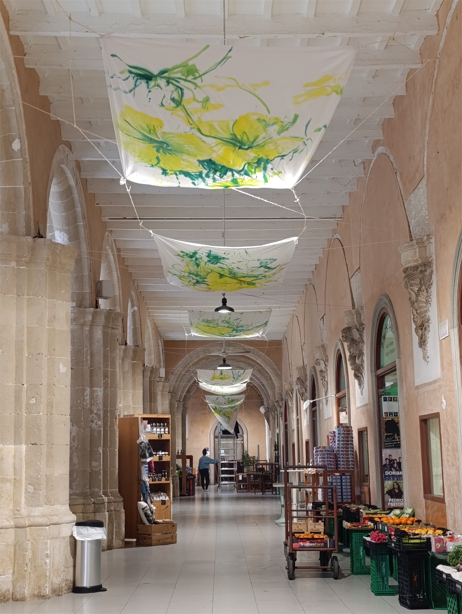 Vista del passadís amb teles pintades de flors verdes i grogues suspeses al sostre